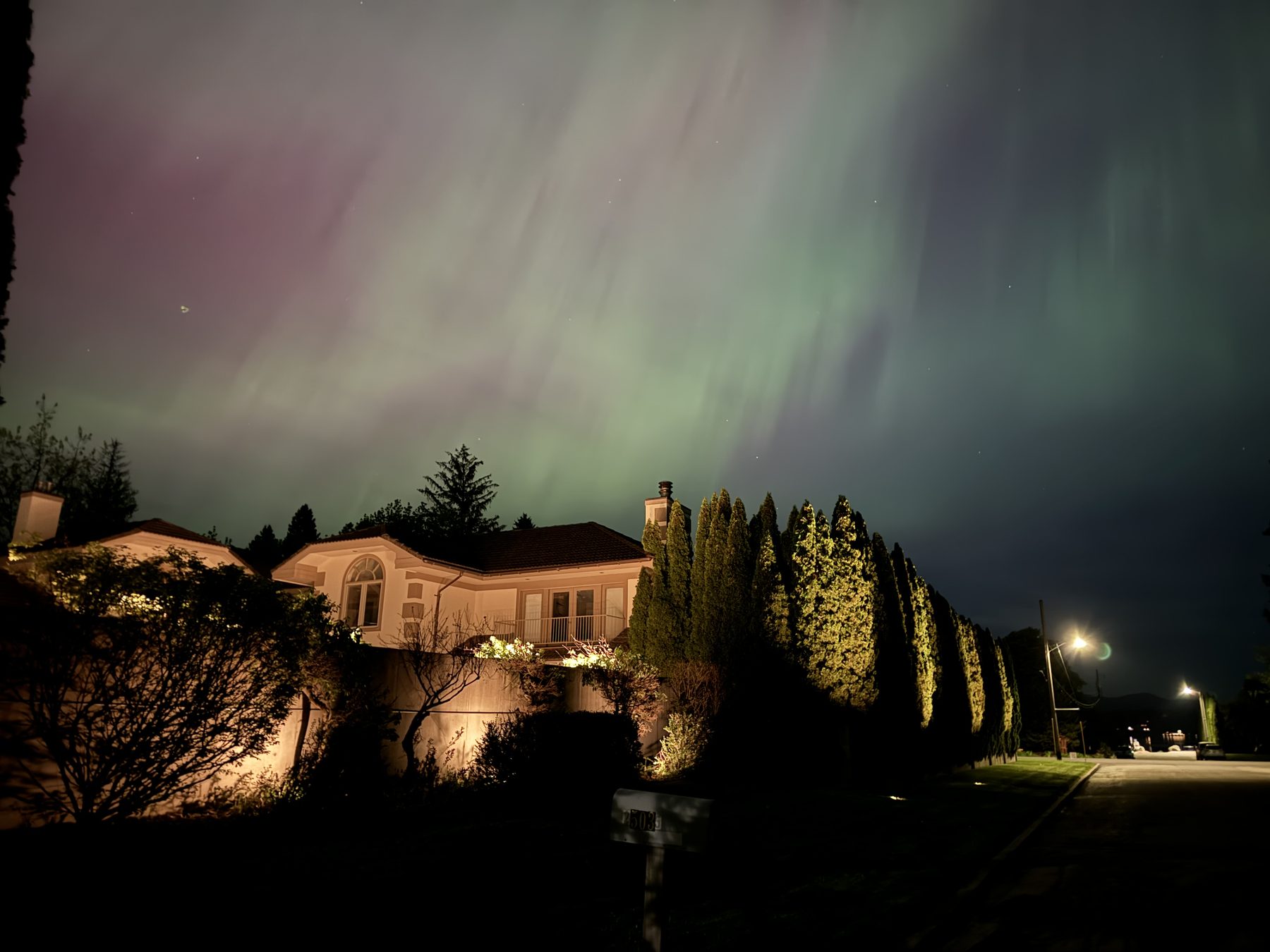 North Idaho home illuminated against aurora borealis — landscape uplighting Sandpoint Idaho